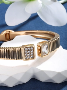 Close-up of golden open bangle featuring a large square gemstone and pave set zirconias