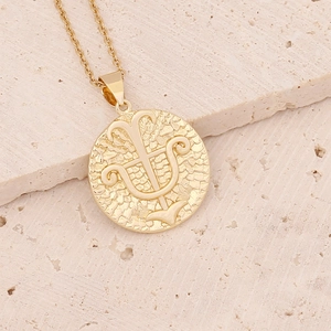 Macro shot of 18K gold zodiac pendant with trident relief on textured coin necklace