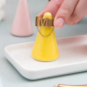 Golden letter M ring with mesh band displayed on a yellow cone jewelry stand