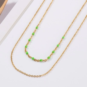 Détail d'un collier doré double épaisseur avec perles vertes et chaînes en acier poli