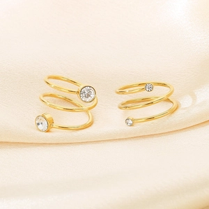 Detail shot of gold spiral open rings with clear crystals on a beige silk background