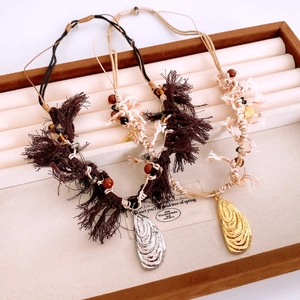 Detail of woven rope necklace with gold and silver shell pendants on velvet display