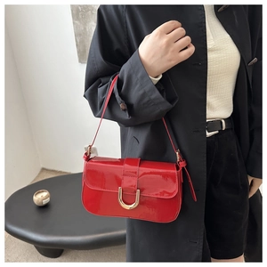 Red patent leather shoulder bag with gold horseshoe buckle worn with a black trench coat