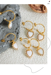 Detail of gold heart earrings with white mother-of-pearl and pearls on natural stone