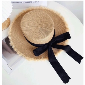 Detail of flat top straw boater hat featuring frayed edges and black ribbon bow accent