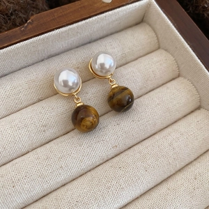 Close-up of gold pearl earrings with tiger's eye pendants in a beige jewelry box
