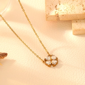 Close-up of gold clover necklace with four heart-shaped crystals on beige leather