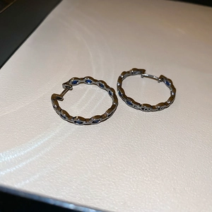 Detail of silver hollow hoop earrings featuring inset round blue sapphire stones