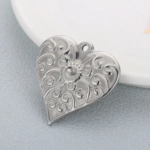 Intricate silver heart pendant with floral engraving and scrollwork on grey surface
