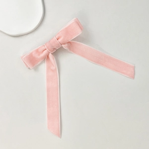 Close-up of pink velvet bow hair clip with long ribbons on a minimalist background