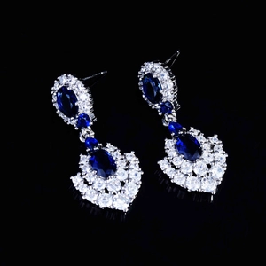 Macro view of royal blue sapphire earrings with brilliant diamond accents on black surface