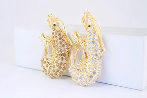 Detailed view of twin gold shrimp pendants encrusted with brown and white rhinestones