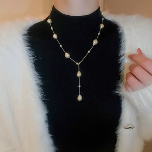 Macro detail of Y-shaped gold plated necklace with baroque pearls on a black sweater