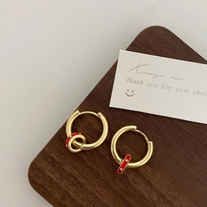 Detail of gold hoop earrings with red enamel charms on a walnut wood surface
