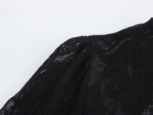 Détail du tissu en dentelle noire montrant le motif floral ajouré et la couture d'épaule