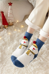 Close-up of fluffy snowman socks with blue heels on white blanket with festive lights