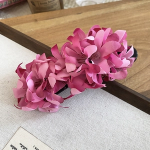 Detail of pink fabric flower hair clip with layered petals on a natural wooden background