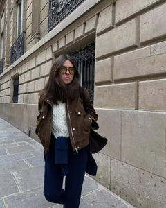 Dettaglio della giacca scamosciata marrone scuro con cerniera e maglione bianco a trecce