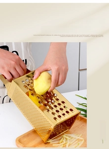 Macro shot of 4-sided gold stainless steel box grater slicing fresh potato