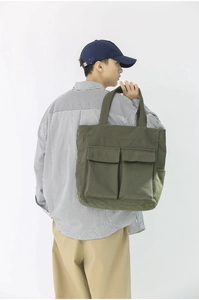 Army green canvas tote bag with front pockets shown on shoulder for capacity and fit