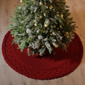 Jupe de sapin de Noël en tricot rouge avec motif torsadé sur un sol en bois
