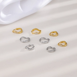 Detail of wave shaped hoop earrings with small zircon stones in silver and gold finish