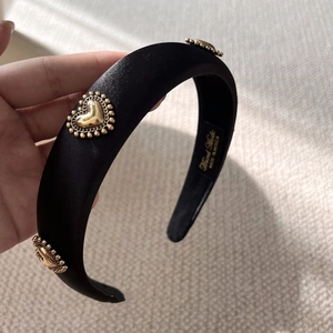 Close-up of black satin padded headband with gold heart metal ornaments and brand engraving