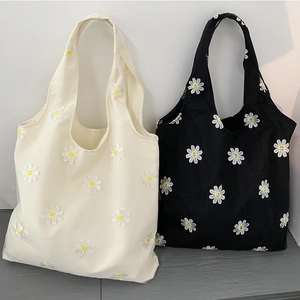 Close-up of daisy embroidery and fine canvas texture on white and black tote bags