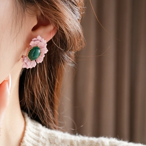 Detail view of pink flower earrings with green oval gemstone on a female model
