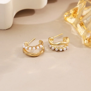 Macro detail of gold double-layer C-shaped hoop earrings with white pearls