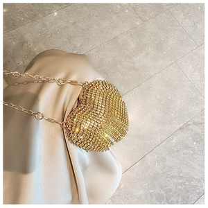 Detailed close-up of a golden heart-shaped evening bag with shimmering rhinestones and chain