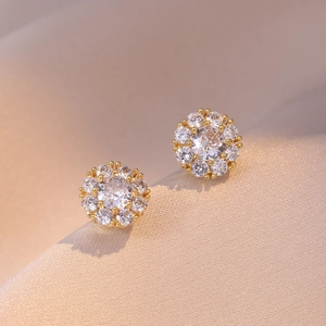 Pendientes de flores doradas con circonitas blancas brillantes sobre seda beige