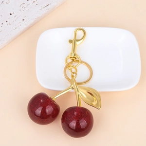 Close-up of glittery dark red cherry keychain with polished gold metal leaf and ring