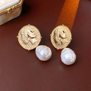 Detailed close-up of vintage golden coin earrings with large irregular pearl drops