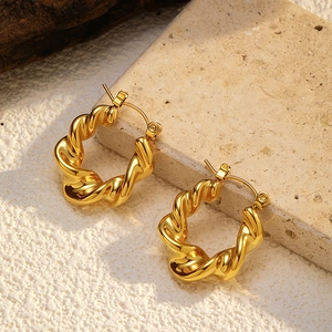 Close-up of golden stainless steel twist hoop earrings on natural stone background