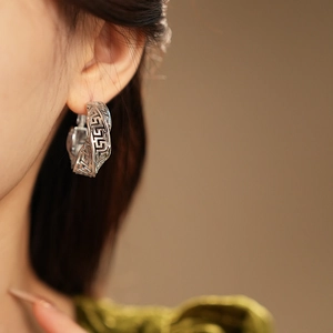 Detailed close-up of a silver-toned twisted earring with an intricate hollow Greek pattern