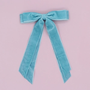 Detail of teal blue velvet hair clip with long double ribbons on pink backdrop