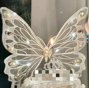 Detailed view of a white lace butterfly cake topper with pearls, rhinestones and a candle