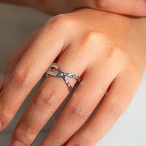 Macro shot of silver X-shaped stainless steel ring with hammered texture on a hand