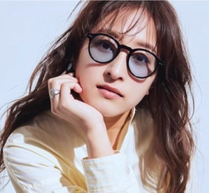 Close-up of black round sunglasses with light blue lenses worn by a model in soft lighting