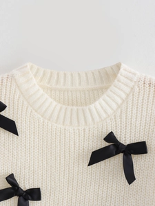 Gros plan détaillé du pull en maille crème avec des nœuds décoratifs en satin noir