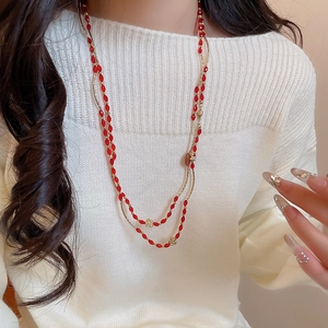 Detail of red bead long necklace with golden floral accents on white knit sweater