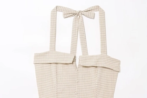 Detail of checkered halter neck top with bow straps and button-down front on white background