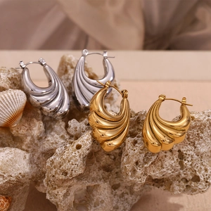 Detail shot of gold and silver hoop earrings with wavy textures on coral rocks