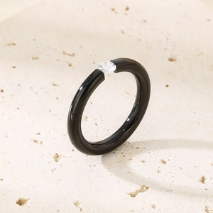 Macro view of a black high-gloss band ring with a round clear zircon on stone background