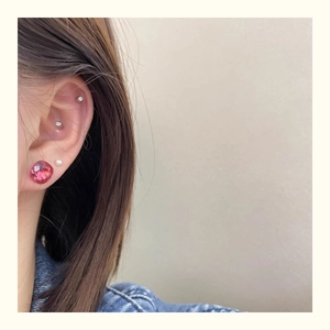 Detail of pink crystal stud and pearl earrings worn on ear with silver helix piercings