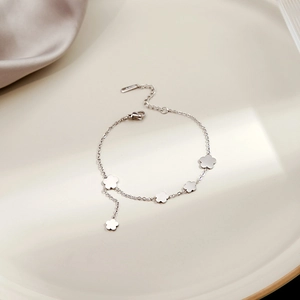 Detailed view of silver flower charm bracelet with lobster clasp on ceramic plate