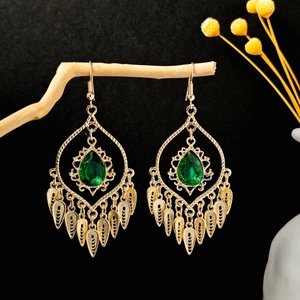 Close-up of vintage gold tassel earrings with green teardrop stone on wooden branch