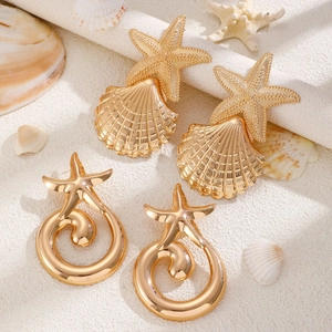Detailed view of golden starfish and seashell stud earrings on a sandy beach background