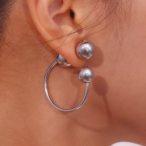 Close-up of silver geometric hoop earrings with three metal spheres worn on the ear